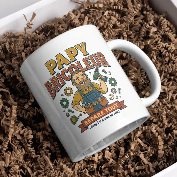 Mug en céramique blanche avec une illustration de dessin animé colorée d’un homme barbu en salopette tenant des outils, avec le texte « papy bricoleur » et « repaire tout (sauf les maux de tête) » imprimés dessus