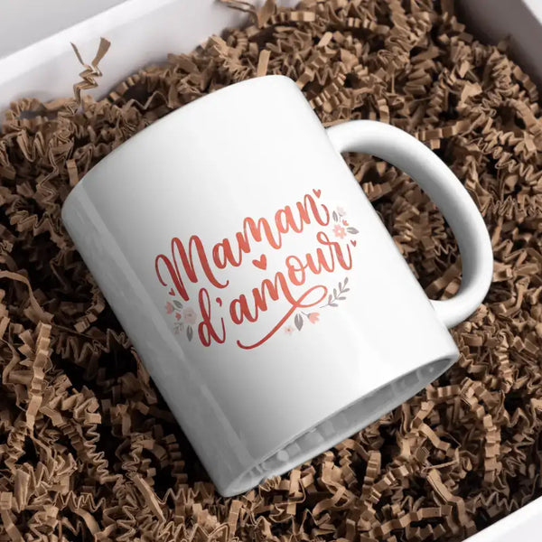 Tasse en céramique blanche ornée de la phrase « maman d’amour » en script élégant en or rose, décorée de motifs floraux et cœurs délicats.